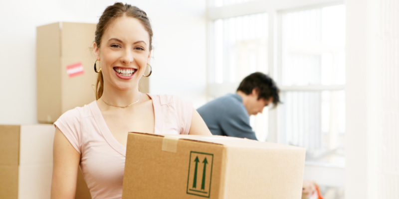 A Smiling Woman With Cardboard Box In Busy Relocating Work.