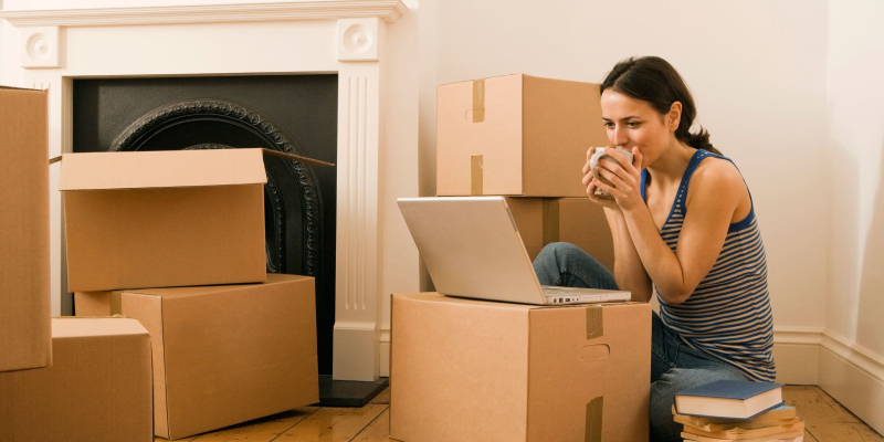 A Woman Having Coffee While Watching Her Laptop During The Relocation.