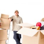 A Woman With Box Full Of Relocation Stuffs & Packers Standing On The Background.