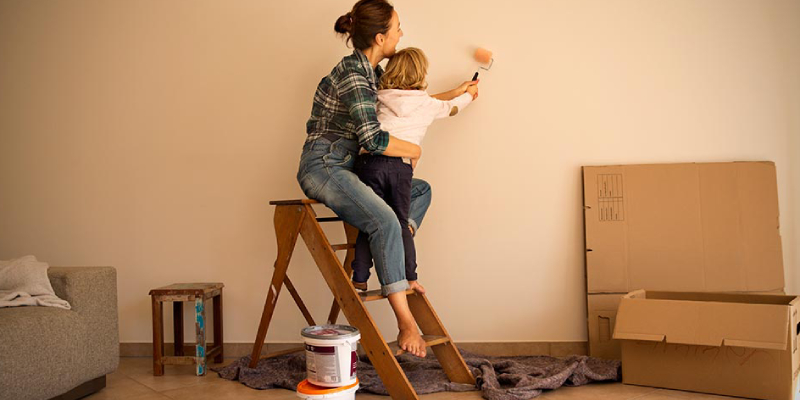 A Small Kid With His Mother Painting The Wall & Relocation Stuffs Beside them.