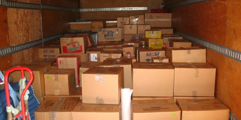 A pile of cardboard boxes in various shapes placed inside a moving truck with the brown wooden walls.