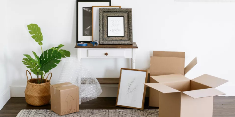 A draw table containing art frame works and Cardboard boxes scattered in floor with other accessories like tape, scissors and marker pen for packing