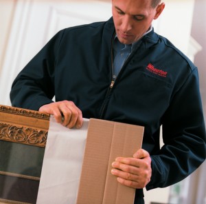 A man in black jerkin packing a framed art work inside a cardboard box